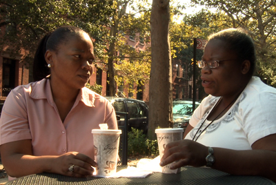 A photo of a person with DD and a staff person talking as if discussing options outside of a coffee shop.